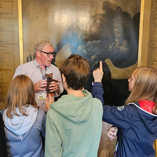 Gids vertelt aan kinderen bij een muurschildering