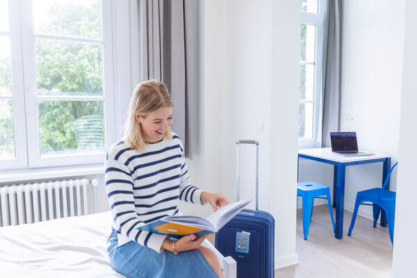 Une hôte lit sur son lit à côté de sa valise