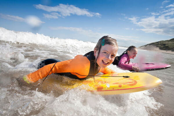 Kinderen bodyboarden in de branding